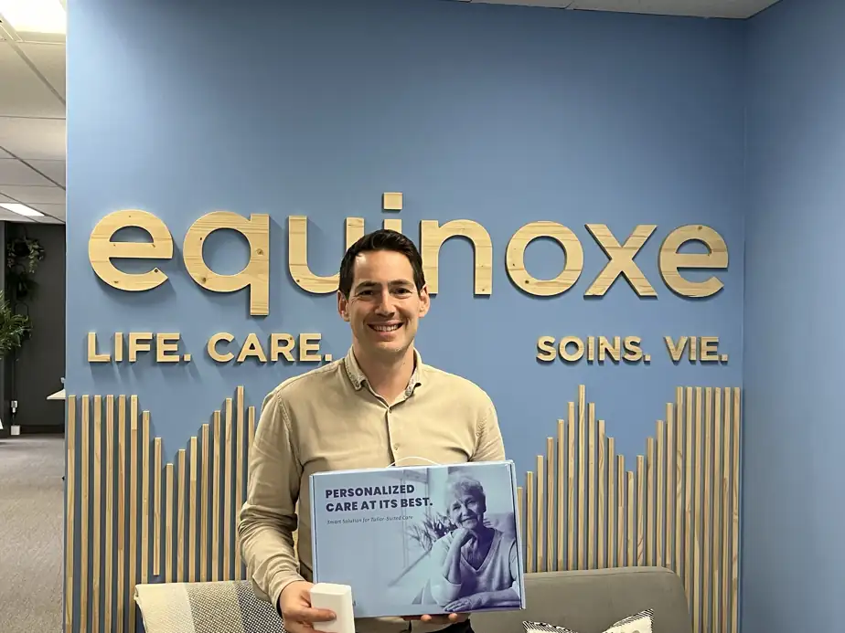 Jeremy Altman, managing director of Equinoxe LifeCare is holding the Equinoxe LifeCare Plus smart home care device in front of the Equinoxe logo while announcing the acquisition of SE Health Quebec operations.